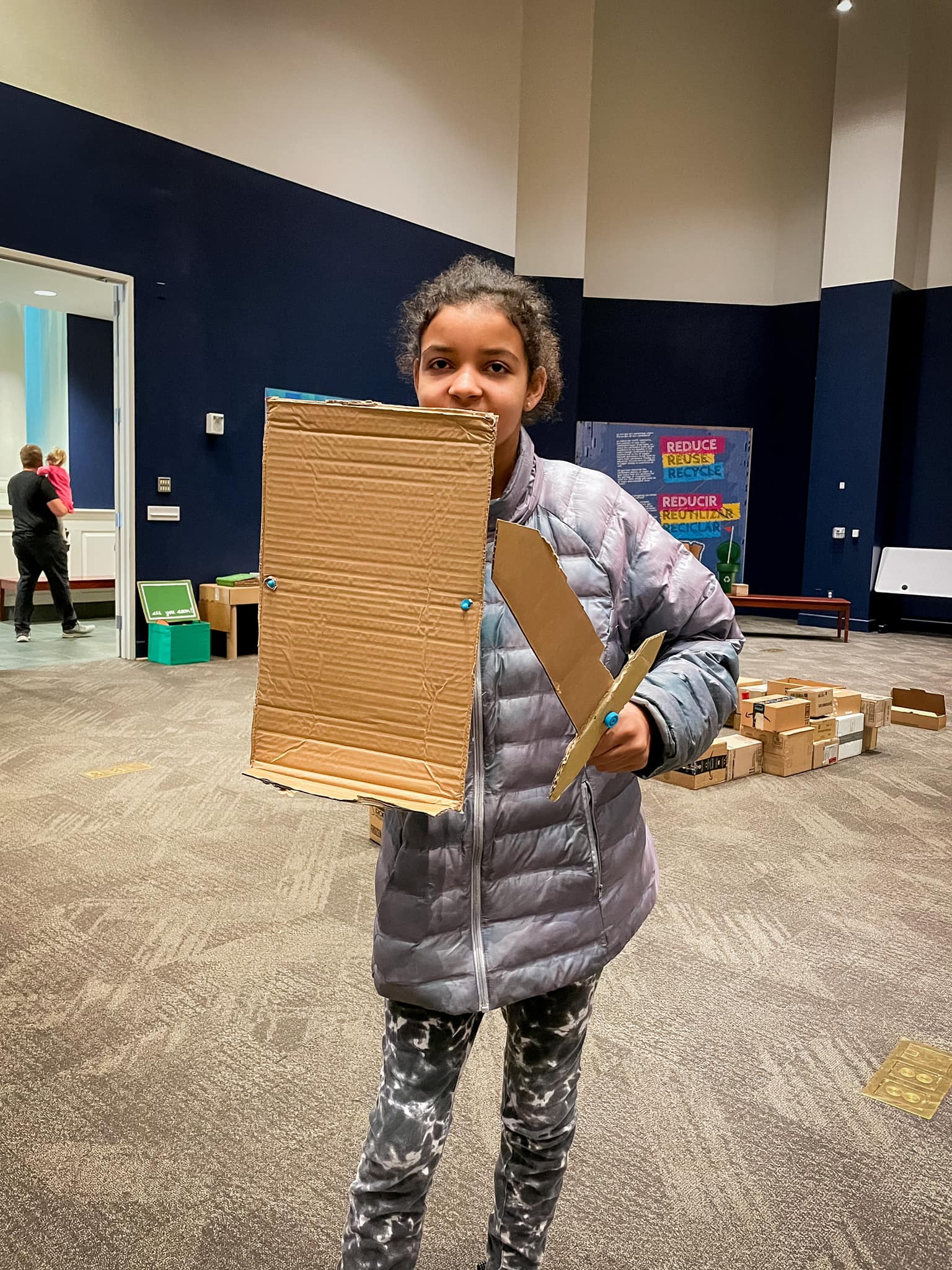 Young girl holding a cardboard shield and sword she created in Cardboard Craze. 