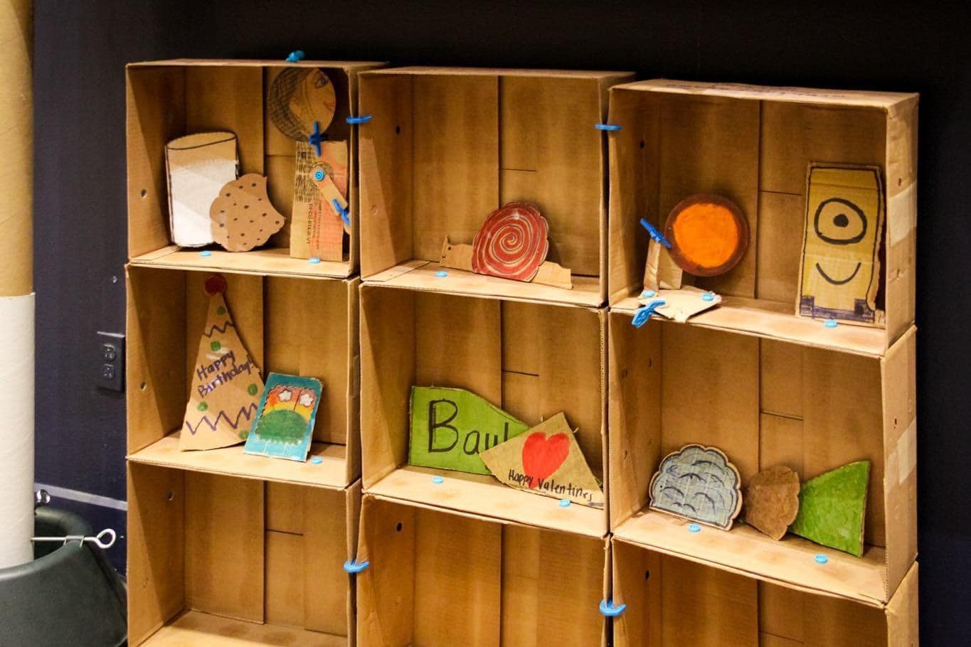 A cardboard bookshelf with cardboard crafts like milk and cookies made of cardboard. 